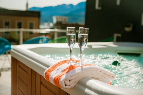 Two glasses of sparkling water sit on a towel by a hot tub, with mountains in the background on a sunny day.