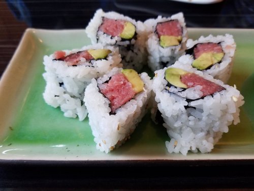 A plate of sushi rolls with tuna and avocado, arranged neatly on a green dish.