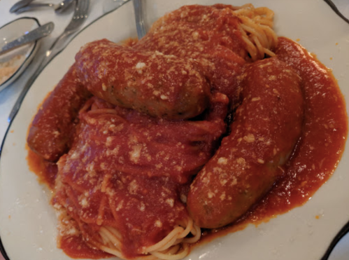 A plate of spaghetti topped with marinara sauce and two large sausages, sprinkled with grated cheese.