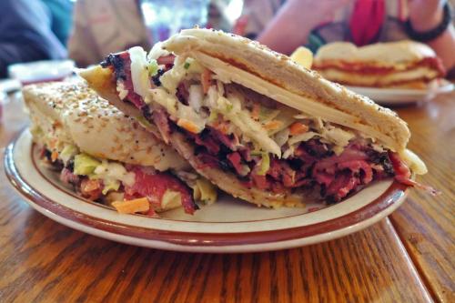 A close-up of a sesame-seed sandwich filled with coleslaw and sliced meat, served on a plate.