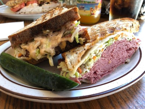 A sandwich with layers of corned beef and coleslaw on toasted bread, served with a pickle on the side.
