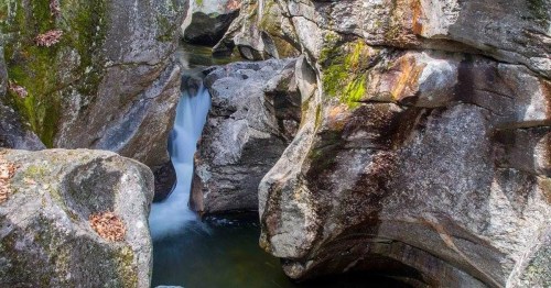 A serene waterfall cascading between large, moss-covered rocks in a narrow canyon.
