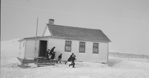 Children playing in the snow near a small white house, with sleds and a snowy landscape in the background.