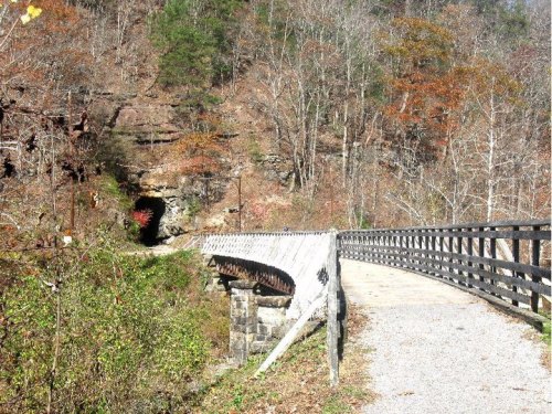 A scenic pathway leads to a tunnel entrance, surrounded by trees with autumn foliage.