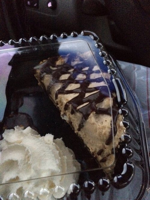 A slice of dessert with chocolate drizzle and whipped cream, placed in a clear plastic container.