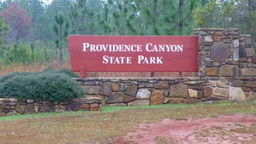 Sign for Providence Canyon State Park, featuring a stone base and surrounded by greenery.