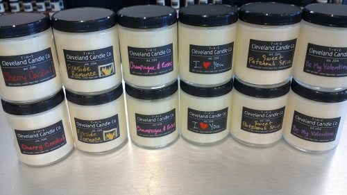 A display of scented candles in jars with colorful labels, featuring various romantic themes and names.