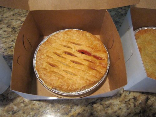 A golden-brown pie with a crisscross pattern, placed inside a cardboard takeout box on a granite countertop.