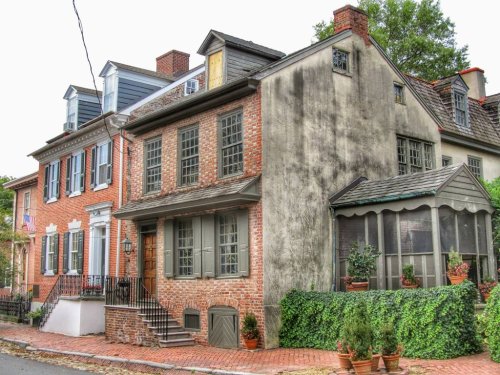 Historic brick houses with greenery, featuring a screened porch and traditional architecture on a quiet street.