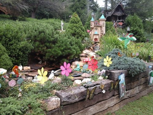 A colorful garden with flower decorations, a small castle, and various plants and ornaments in a lush green setting.