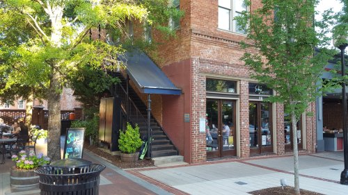 A brick building with a staircase, surrounded by trees and outdoor seating, in a lively urban area.