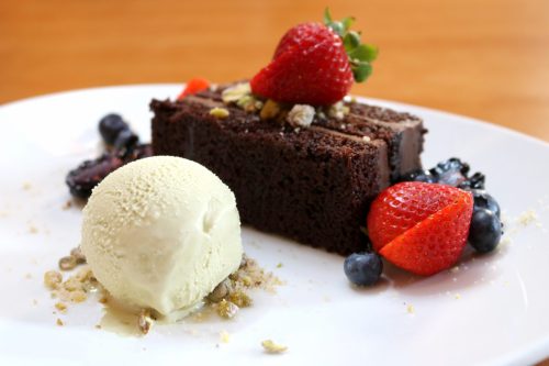 A slice of chocolate cake topped with a strawberry, served with a scoop of vanilla ice cream and fresh berries.