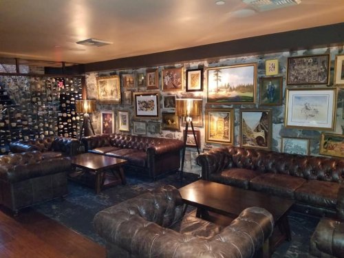 Cozy lounge with leather sofas, wooden tables, and a gallery wall of framed artwork and vintage photos.