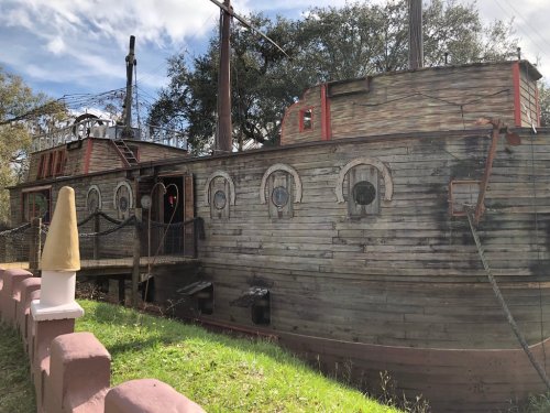A weathered wooden boat with round windows, docked near a grassy area under a blue sky.