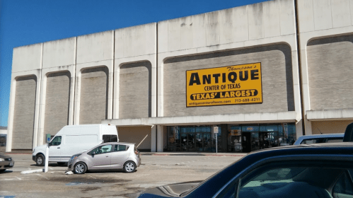 Exterior of Thompson's Antique Center of Texas, featuring a large yellow sign that reads "Texas' Largest." Cars parked in front.