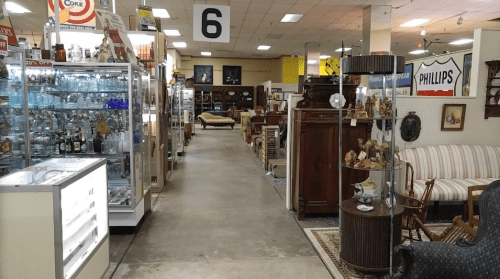A spacious antique store aisle lined with glass display cases and various vintage furniture pieces.