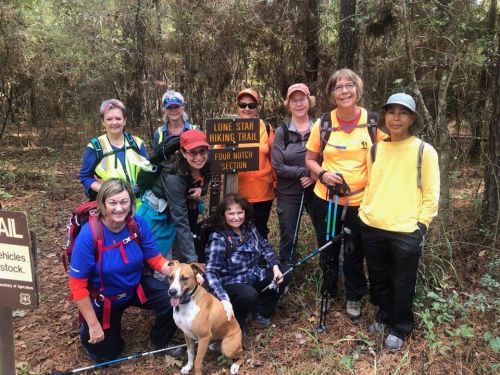 A group of nine hikers, including a dog, pose by a sign for the Lone Star Hiking Trail in a wooded area.