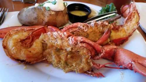 A plate featuring a stuffed lobster tail, baked potato, and a side of dipping sauce.