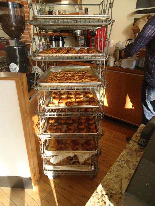 A metal rack filled with various baked goods, including pastries and bread, in a cozy bakery setting.