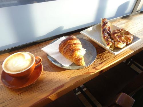 A cup of coffee next to a croissant and two pastries on a wooden table by a window.