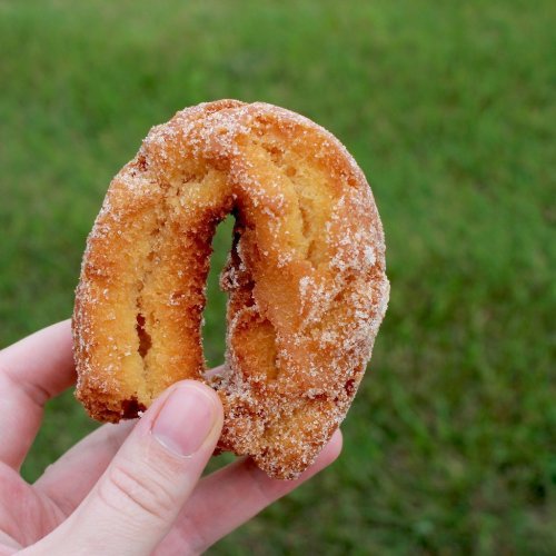 A hand holds a sugar-coated donut shaped like a horseshoe against a green background.
