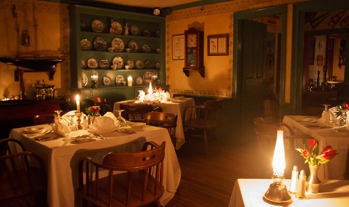 Cozy restaurant interior with candlelit tables, decorative plates on the wall, and a warm, inviting atmosphere.