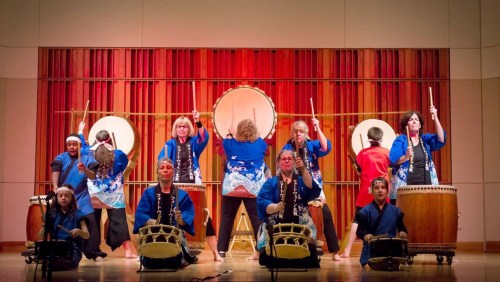 A group of performers in blue outfits playing traditional drums on stage, showcasing a vibrant cultural performance.