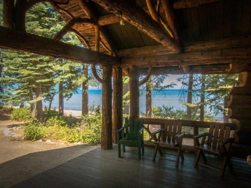 View from a rustic cabin porch overlooking a lake, surrounded by tall trees and a sandy beach.