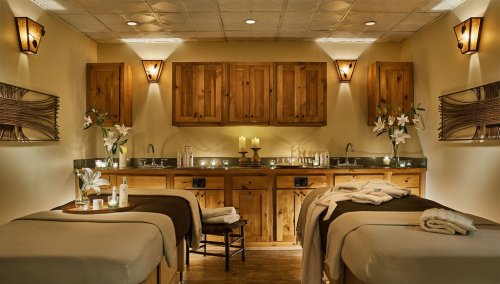 A serene spa room with two massage tables, soft lighting, candles, and wooden decor, creating a calming atmosphere.