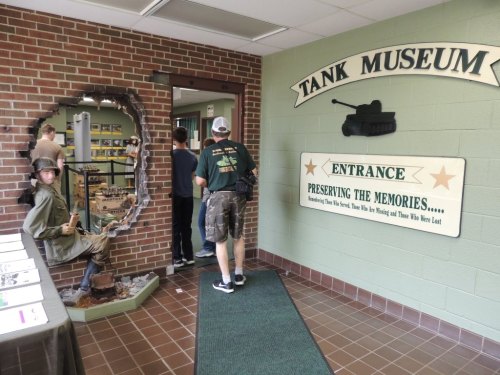 Entrance to a tank museum featuring a soldier statue and visitors entering through a brick wall.