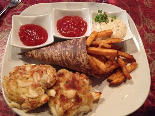 A plate featuring crab cakes, fries in a cone, and three dipping sauces: two ketchup and one creamy sauce.