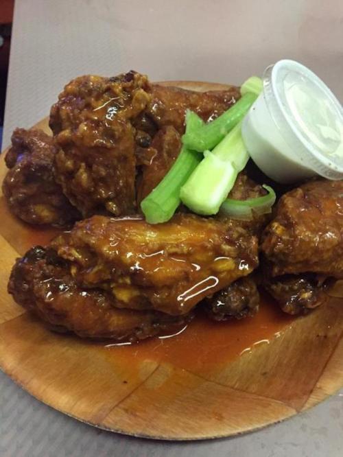 A plate of saucy chicken wings garnished with celery and a small cup of dipping sauce.