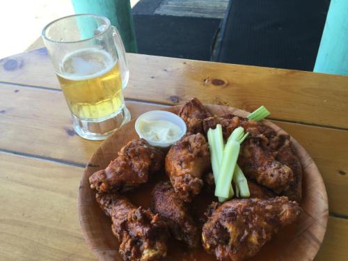 A plate of crispy chicken wings with celery sticks and dipping sauce, alongside a glass of beer on a wooden table.