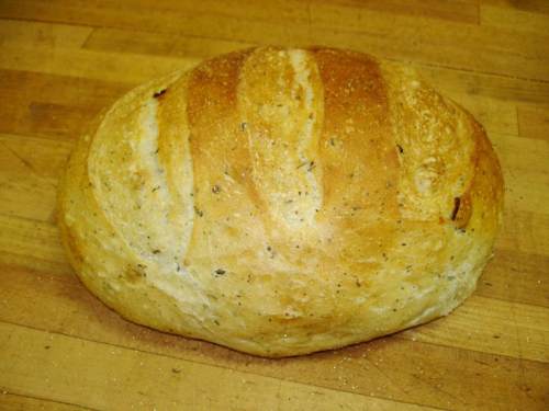 A round loaf of bread with a golden crust and visible scoring on top, resting on a wooden surface.