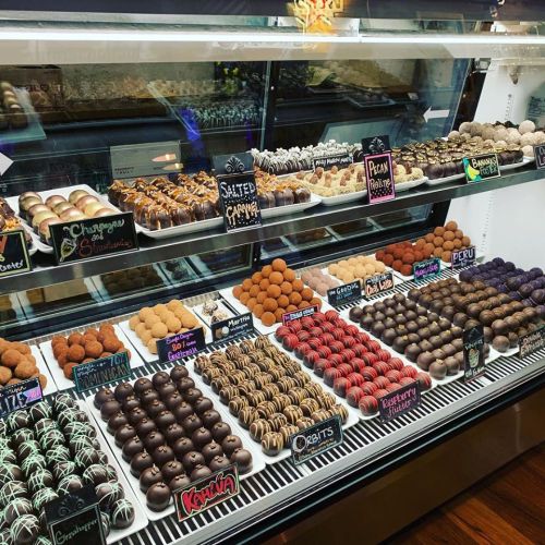 A display case filled with various chocolate truffles and confections, labeled with flavors like salted caramel and pecan praline.