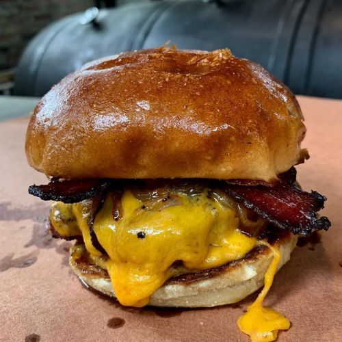 A juicy cheeseburger with melted cheddar, crispy bacon, and caramelized onions on a toasted bun, resting on parchment paper.