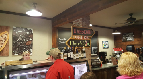 A cozy barbecue restaurant interior with a menu sign, customers at the counter, and various food items displayed.