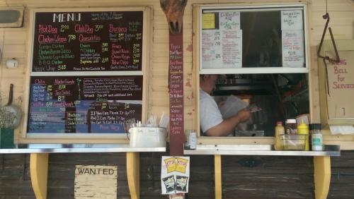 A food truck menu board with various items listed, and a person inside taking orders. Brightly colored and inviting.