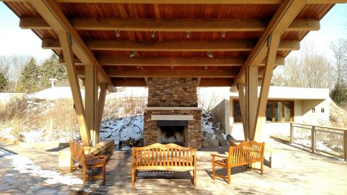 A cozy outdoor seating area with wooden benches and a stone fireplace, surrounded by snow-covered ground and trees.