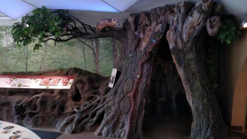 A large, textured tree sculpture with a small animal figure on a branch and an entrance carved into the trunk.