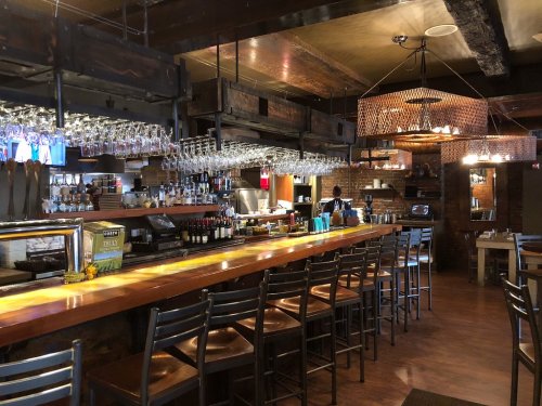 A cozy bar area with wooden accents, hanging glassware, and a warm ambiance, featuring a long counter and seating.