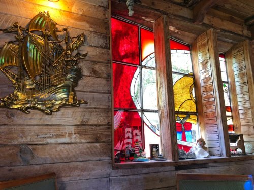 A wooden wall featuring a ship plaque and colorful stained glass windows with nautical themes.