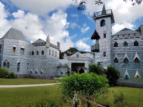 A whimsical castle covered in shiny silver material, surrounded by greenery and under a partly cloudy sky.
