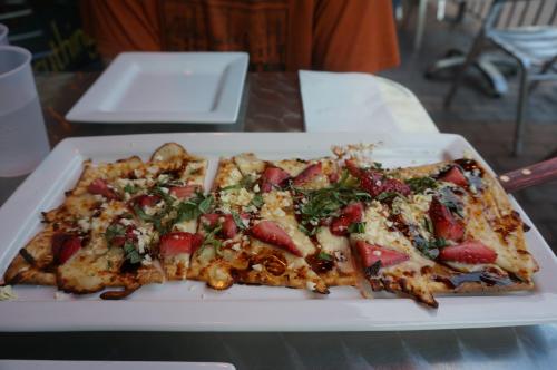 A rectangular flatbread topped with cheese, strawberries, herbs, and drizzled with balsamic glaze on a white plate.