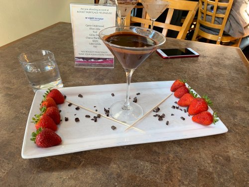 A chocolate martini on a plate with fresh strawberries and chocolate chips, alongside a glass of water.