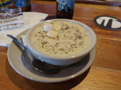 A bowl of creamy soup topped with crackers and black pepper, placed on a wooden table.