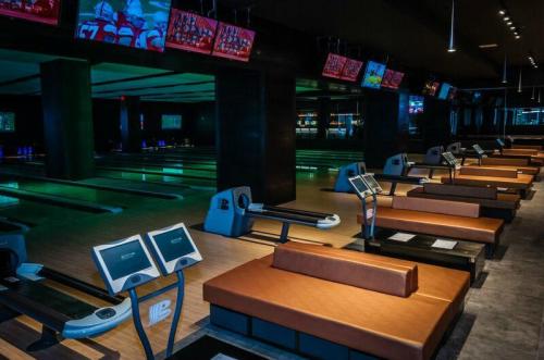 A modern bowling alley with sleek lanes, seating areas, and screens displaying sports events.