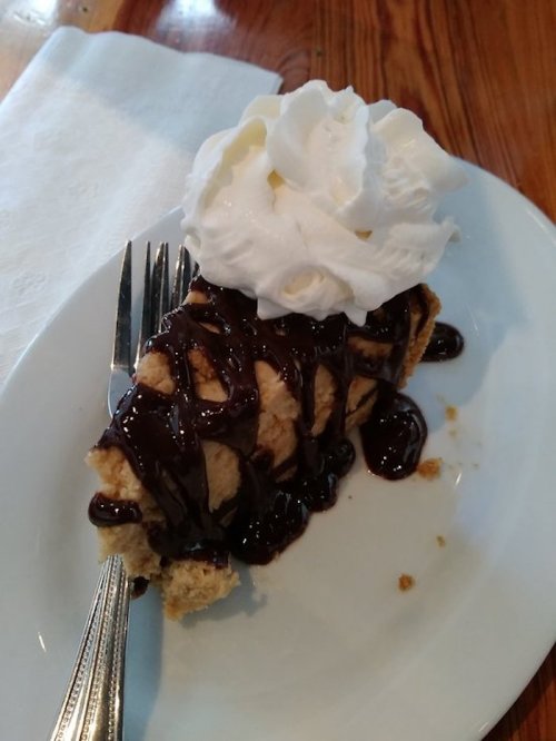 A slice of dessert topped with whipped cream and chocolate drizzle on a white plate, with a fork beside it.