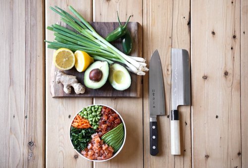 Fresh ingredients for a meal: green onions, jalapeños, ginger, avocados, lemon, and a bowl of colorful vegetables and fish.