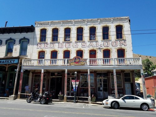 Historic Red Dog Saloon building with a balcony, surrounded by shops and parked cars under a clear blue sky.
